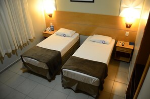 Ein Hotelzimmer mit zwei Einzelbetten, einem Nachttisch mit Lampe, einem Telefon und einem kleinen Beistelltisch.