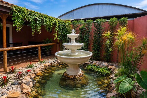 Une fontaine à plusieurs niveaux, située dans un jardin avec un mur rouge et de la verdure.