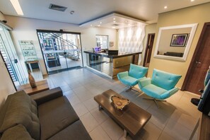 Un hall d’hôtel moderne avec un canapé, des fauteuils, une table basse et un escalier menant à l’étage supérieur.