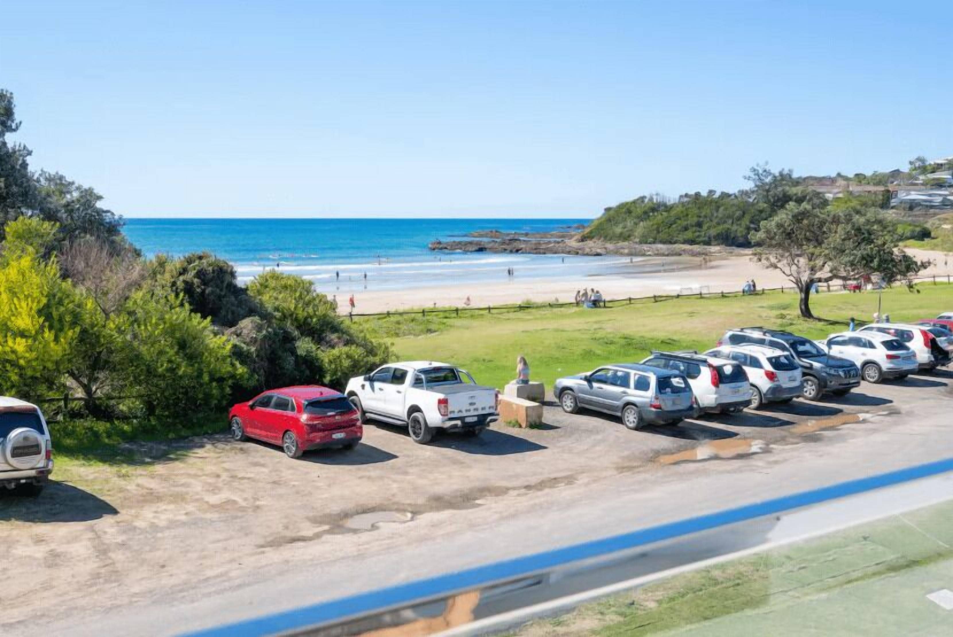 A parking area with vehicles, a beach, and a clear sky.