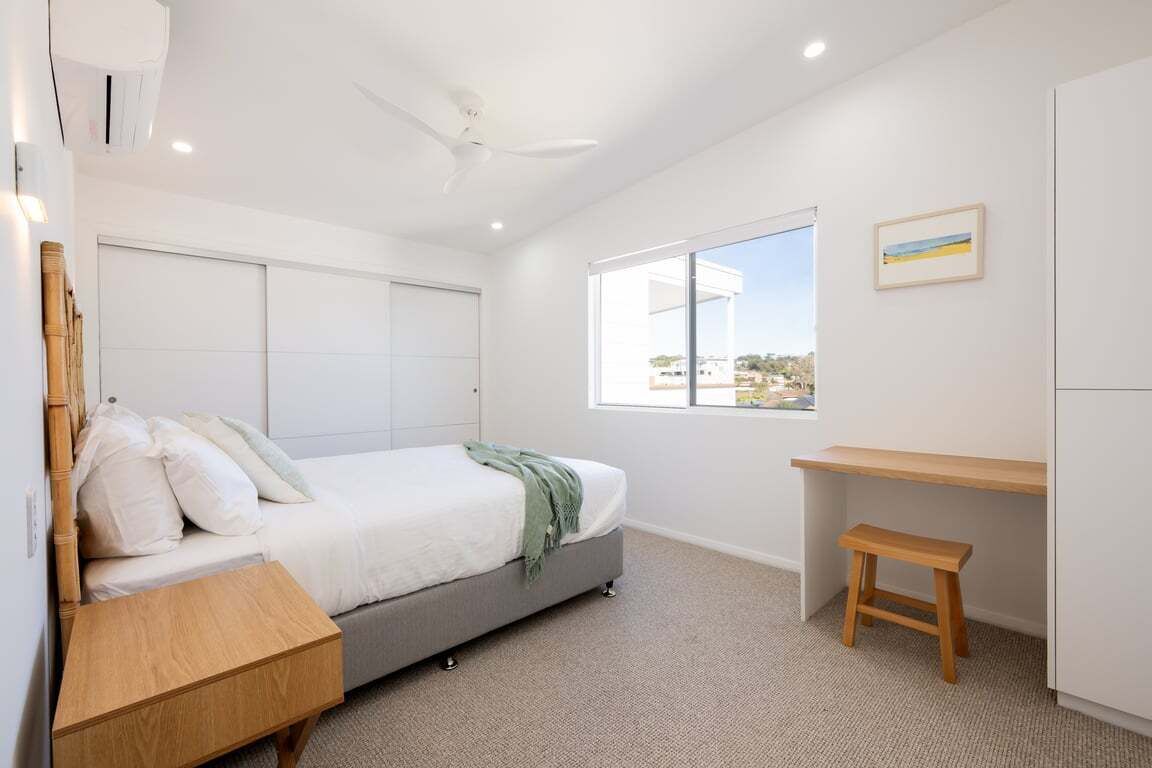 Une chambre à coucher avec un lit, un bureau, une fenêtre et un ventilateur de plafond.