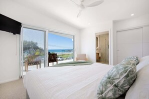 A bedroom with a large bed, a ceiling fan, and a view of the beach through a sliding glass door. - Adrift - Beachfront living on Woolgoolga Beach (Woolgoolga)