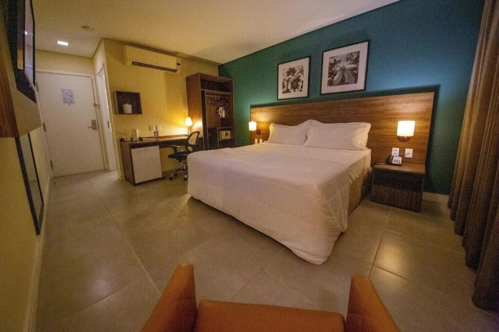 Een hotelkamer met een groot bed, een bureau met stoel, een kledingkast en twee bedlampen.