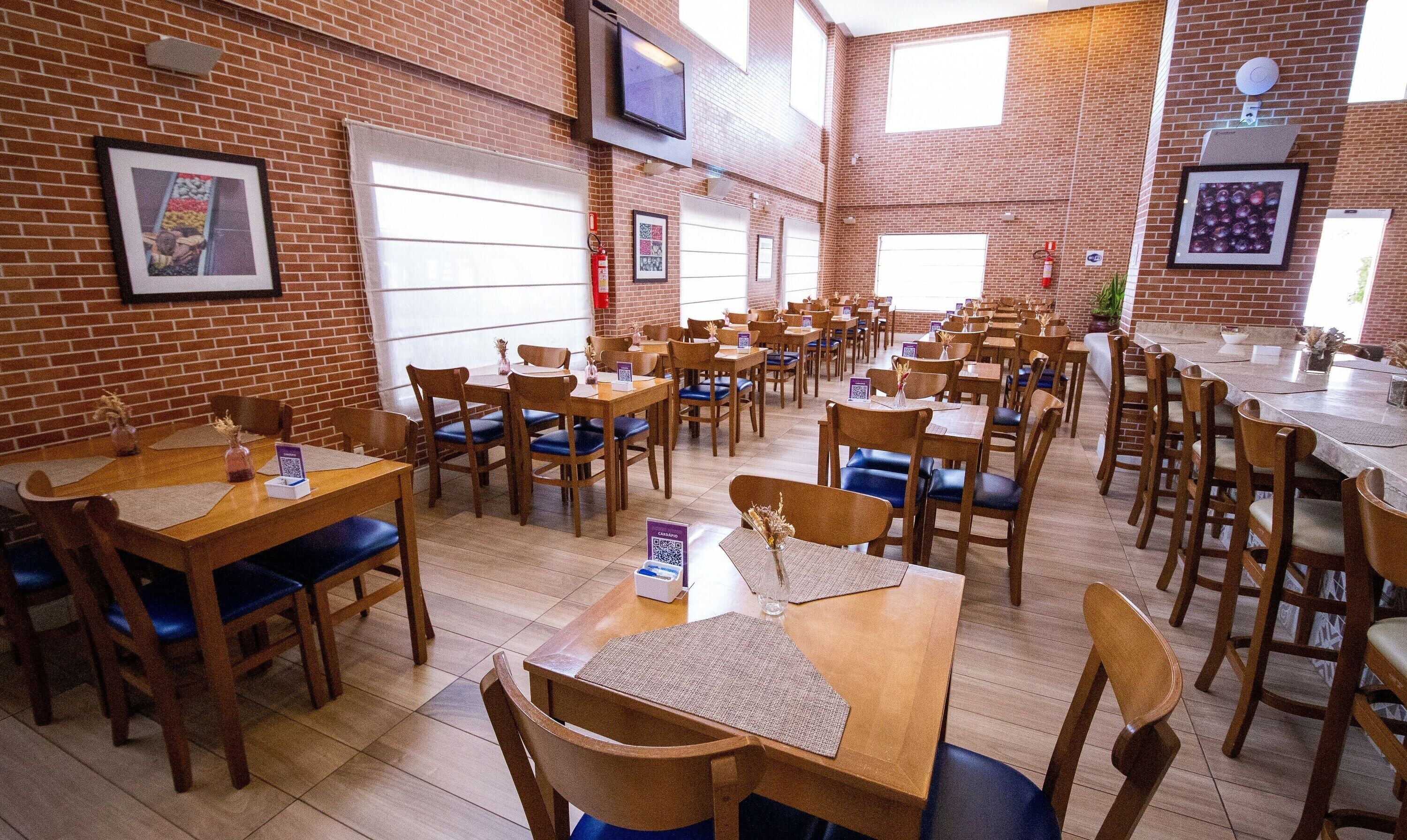 Een restaurant met bakstenen muren, houten tafels en blauwe stoelen met kussens.