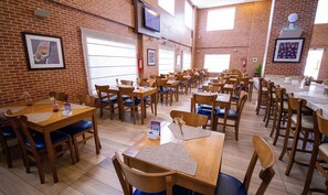 A restaurant with brick walls, wooden tables, and blue cushioned chairs. - Rooftop Evenings, Poolside Days & Comfortable City Stays (Acre)