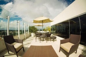 A balcony with a table and chairs, large windows, and a view of the city. - Rooftop Evenings, Poolside Days & Comfortable City Stays (Acre)