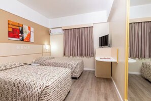 Habitación de hotel con dos camas, televisión, escritorio pequeño y espejo.