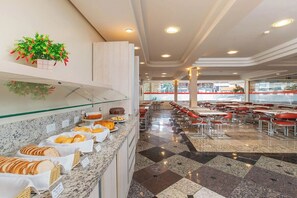 Comedor de hotel con bufé, mesas dispuestas y una planta decorativa.