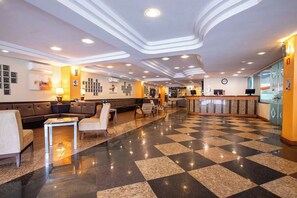 Un vestíbulo de hotel con piso a cuadros, zona de estar, mostrador de recepción e iluminación moderna.