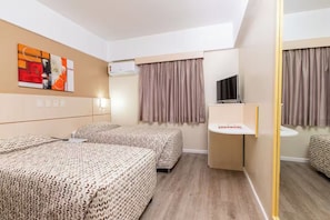 Ein Hotelzimmer mit zwei Betten, einem Fernseher, einem kleinen Schreibtisch und einem Spiegel.