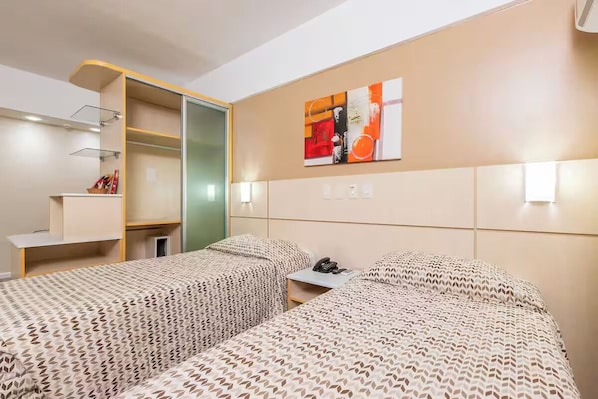Ein Hotelzimmer mit zwei Betten, einem Schreibtisch und einem an der Wand befestigten Fernseher.