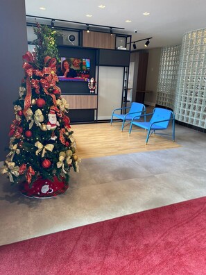Ein Empfangsbereich mit Weihnachtsbaum, blauen Stühlen und einem Fernsehbildschirm.