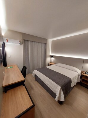 Ein Hotelzimmer mit einem Bett, einem Schreibtisch, einem Sessel, einem Fernseher und einem Nachttisch.