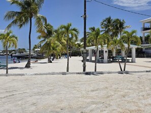 Ein Strand mit Palmen, einem Boot und einem Gebäude mit heller Fassade.