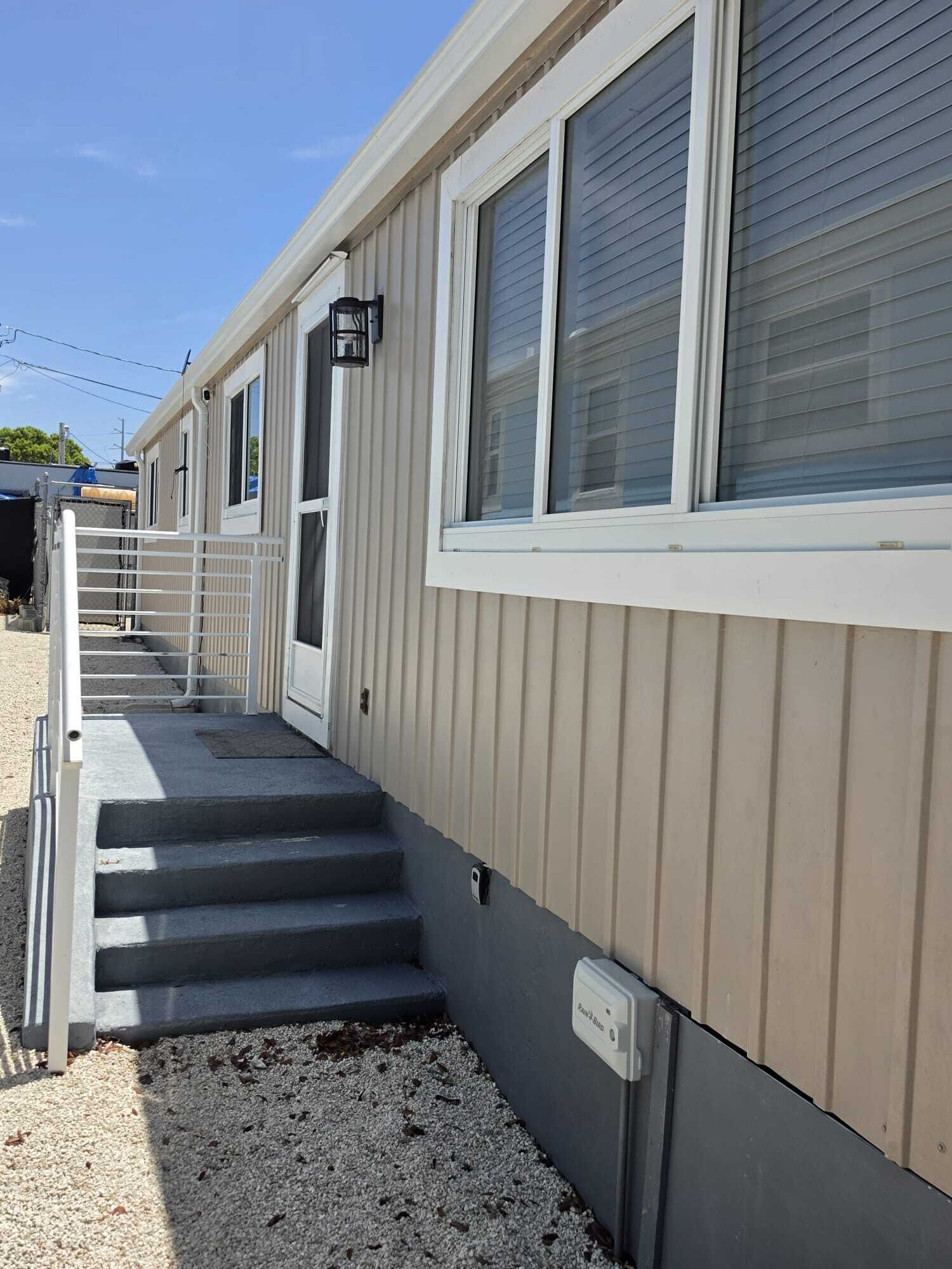 A building with a covered porch, a set of stairs leading to a door, and a utility box on the ground.