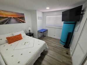 Ein Schlafzimmer mit einem Bett, einem Schreibtisch, einem Fernseher und einem Fenster mit Jalousien.