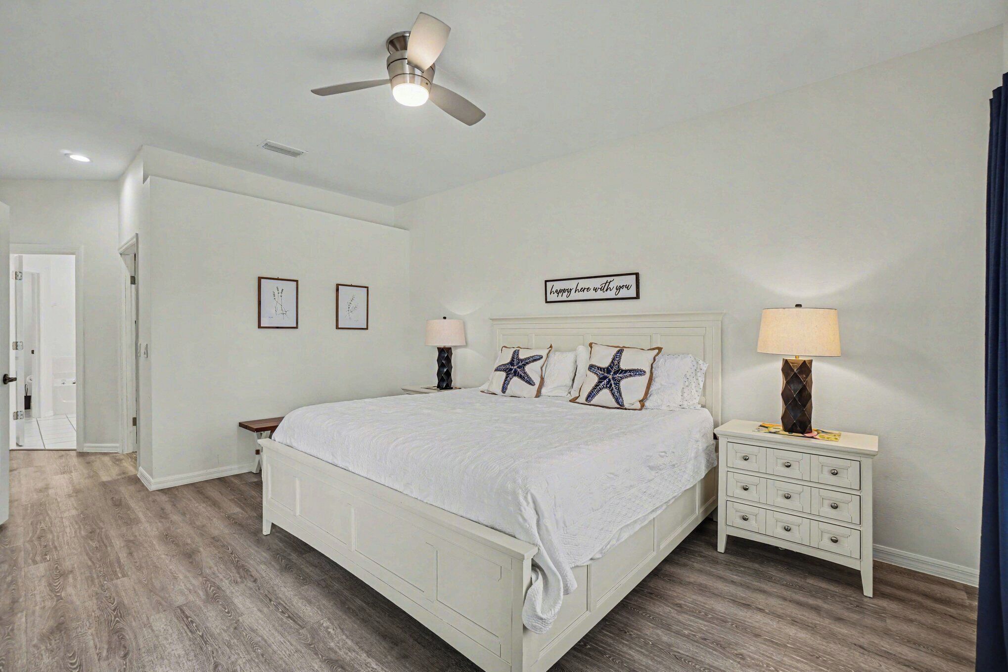 A bedroom with a bed, bedside tables, a ceiling fan, and wall art.