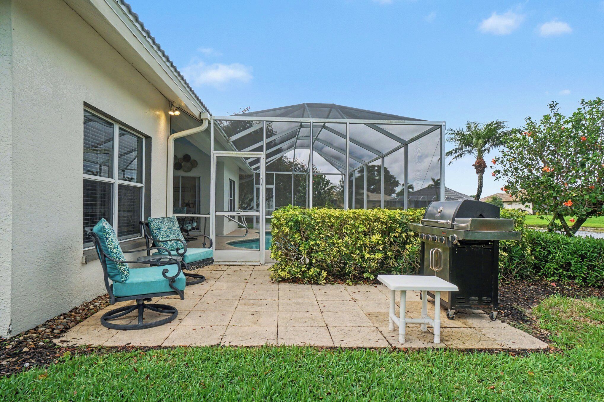 Een overdekte patio met tuinmeubilair, een barbecue en een glazen omheining.