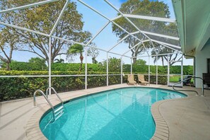 Piscina azul límpida com estrutura de vidro, cercada por um sebedo e árvores.