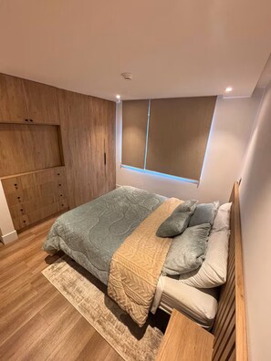 A bedroom with a bed, wooden wardrobe, and a window with blinds. - Modern Apt. with Skyline Views - Easy 5-Min Drive to Center (Cuenca)