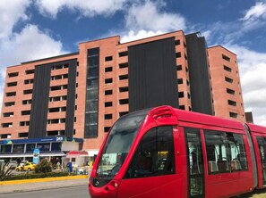 A red tram in front of a multi-story building with a large glass facade and a sign for 'P&S' on the ground floor. - Modern Apt. with Skyline Views - Easy 5-Min Drive to Center (Cuenca)