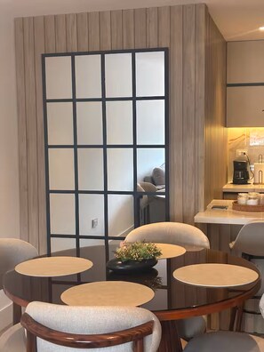 A room with a round table, four chairs, a small plant, and a kitchen area with a coffee maker. - Modern Apt. with Skyline Views - Easy 5-Min Drive to Center (Cuenca)