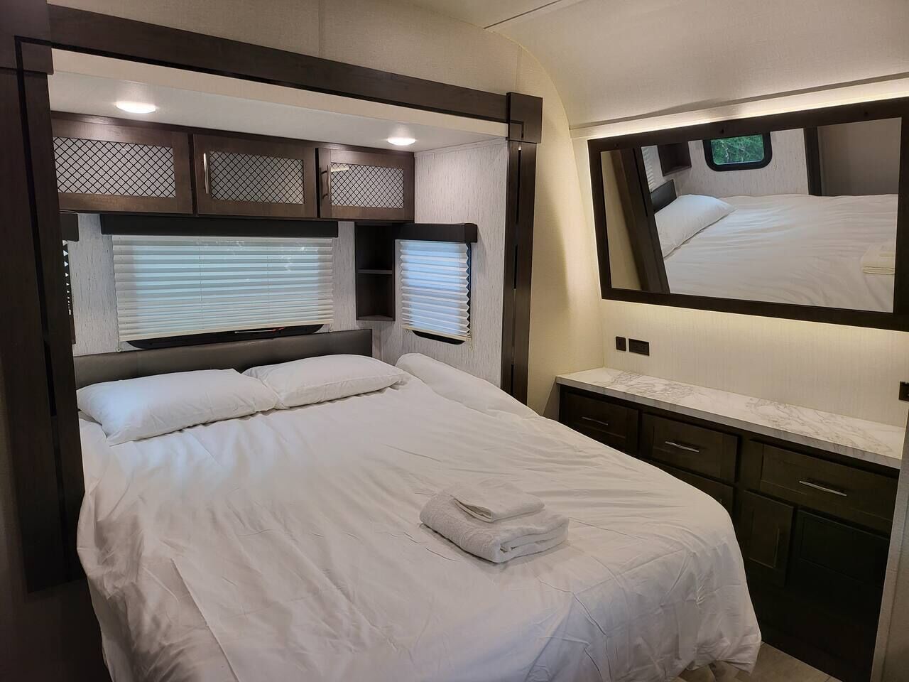 A bedroom with a bed, a mirror, and a window with blinds.