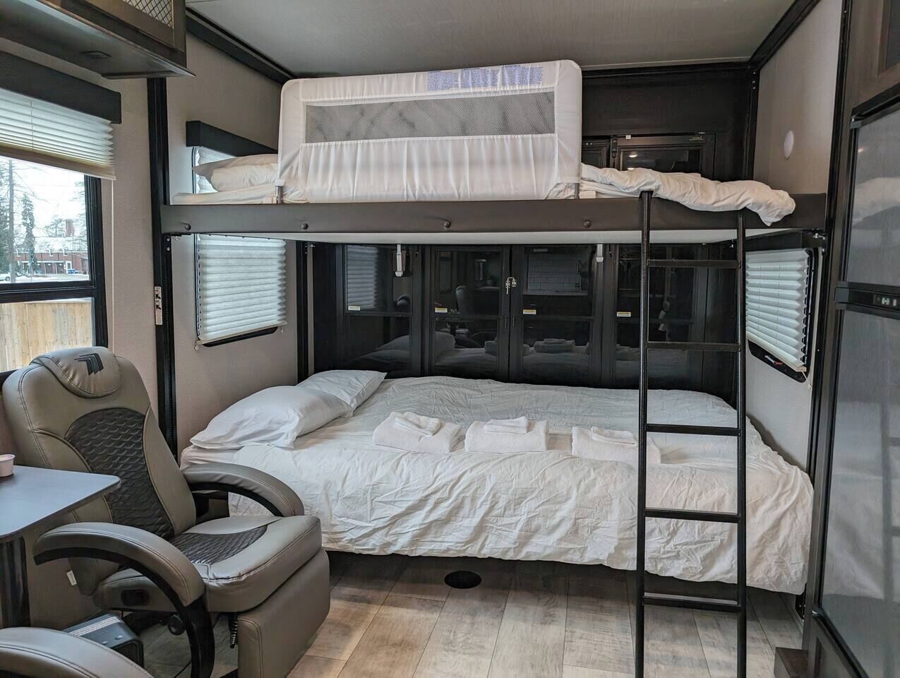 Ein kompaktes Schlafzimmer in einem Wohnmobil mit Etagenbetten, einem kleinen Tisch und einem Stuhl.