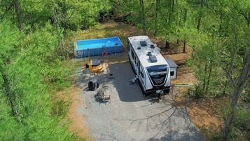A recreational vehicle (RV) parked in a forested area with a swimming pool and outdoor seating.