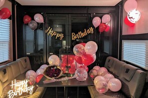 A room with a table decorated for a birthday, surrounded by sofas, and balloons.