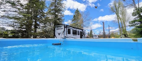 A camper with a swimming pool, surrounded by trees.