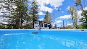 A camper with a swimming pool, surrounded by trees.