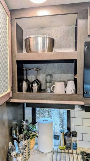 A kitchen with a wooden cabinet, stainless steel bowl, glassware, and utensils.