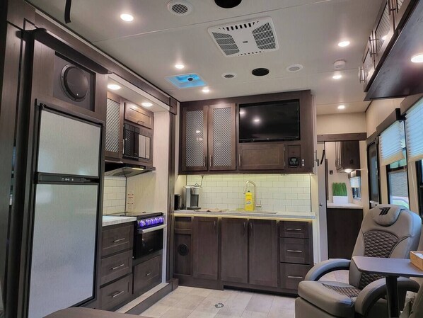 A compact kitchen with a built-in oven, microwave, and a small dining area with a chair.