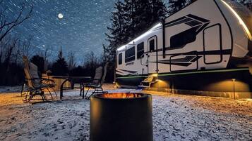 A camper RV parked outdoors at night with a fire pit in the foreground.
