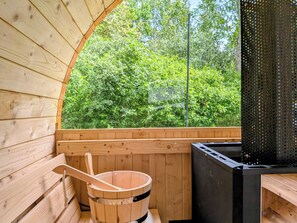 A wooden sauna with a wooden bucket and a black sauna heater.