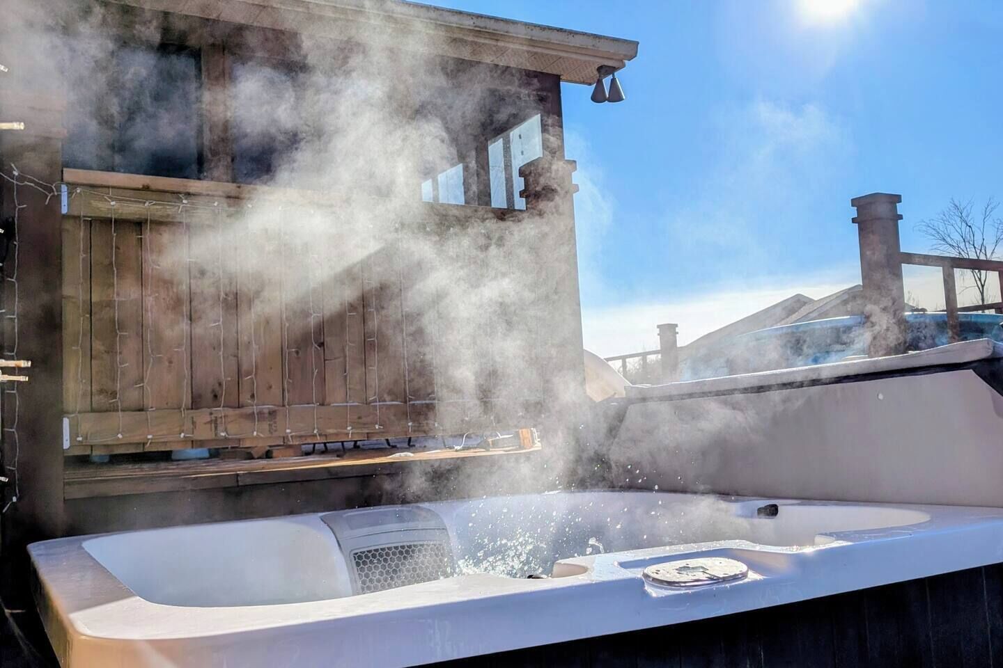 Ein Whirlpool mit aufsteigendem Dampf, eine Holzterrasse und ein klarer Himmel.