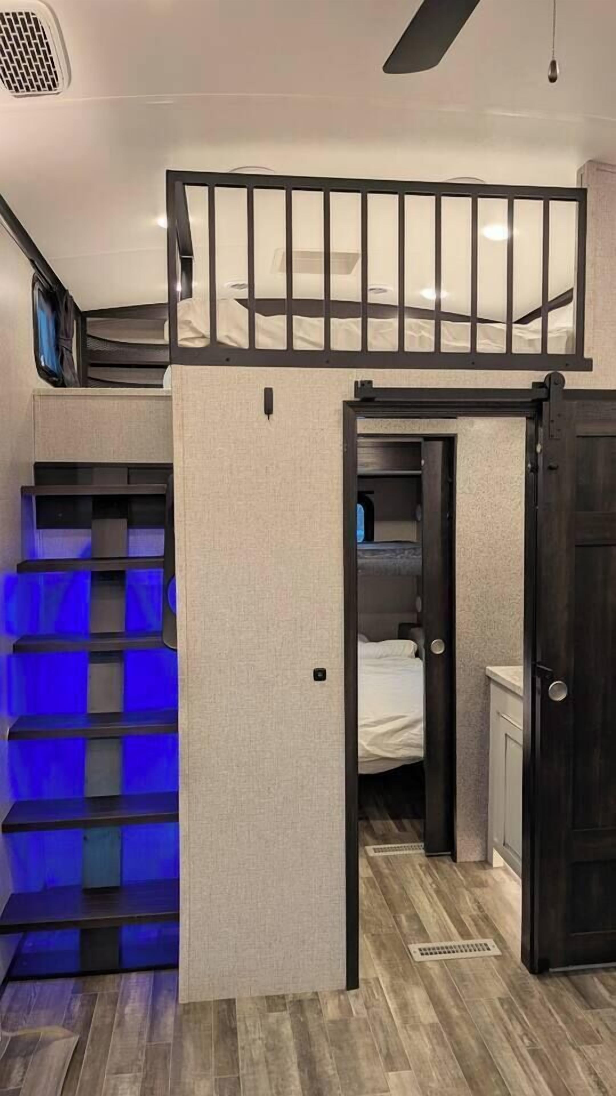 A compact room with a bunk bed, a small desk, and a storage unit with blue lighting.
