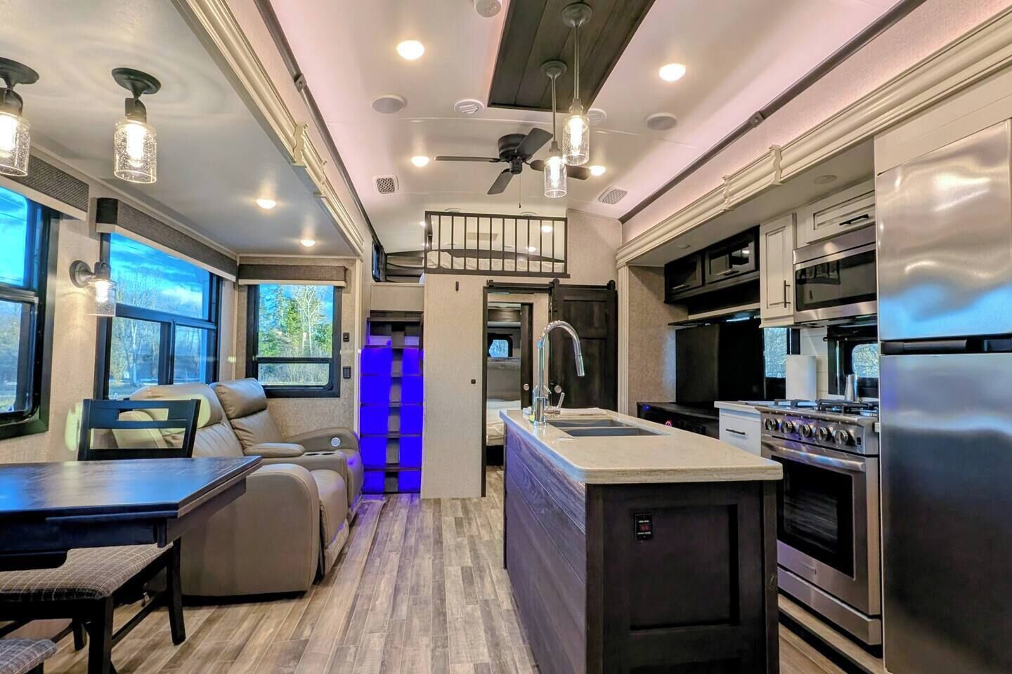 A modern RV interior with a kitchen, dining area, and a seating space with a view.