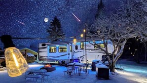 A snow-covered outdoor area with a dining table and chairs, a fire pit, and a large RV with 'North Point' written on it.