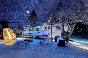 Un espacio exterior cubierto de nieve con una mesa y sillas, una fogata y una gran caravana con la inscripción 'North Point'.