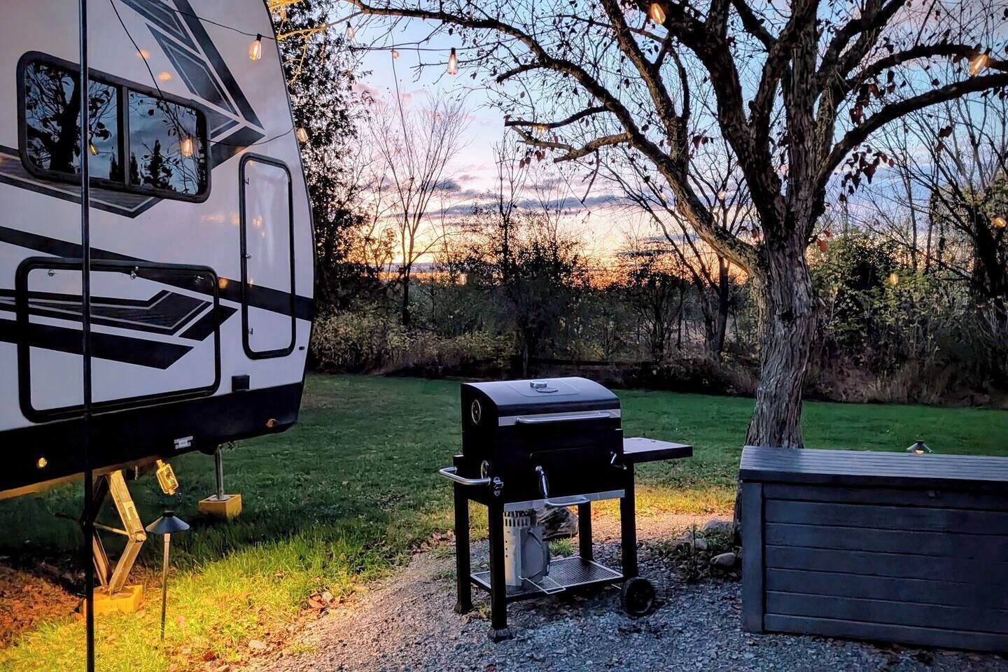 Una caravana estacionada en un área verde con una parrilla y un cobertizo cerca.