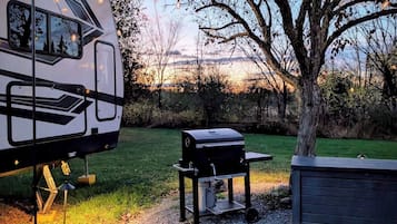 Una caravana estacionada en un área verde con una parrilla y un cobertizo cerca.