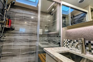 Un baño moderno con ducha envuelta en vidrio, pared con azulejos de mármol e instalación de lavamanos con un práctico revestimiento de baldosas de cuadros.
