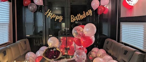 A room with a table decorated for a birthday, surrounded by two sofas, and balloons.