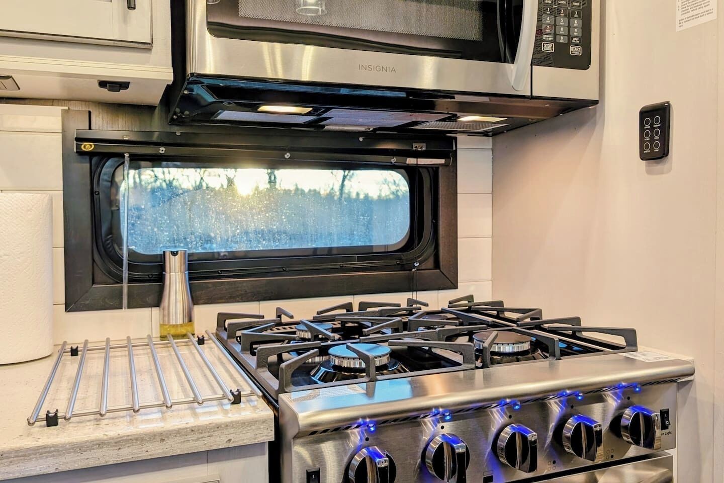 A kitchen with a stainless steel stove, a microwave above it, and a window with a view of trees.