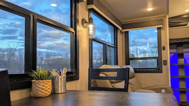 A cozy seating area with a table, a chair, and a window with a view of a cloudy sky.