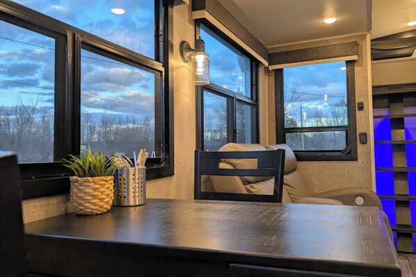 Un rincón acogedor con una mesa, una silla y un ventanal con vistas a un cielo nublado.