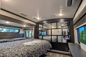 Un dormitorio moderno para vehículo recreativo, con dos camas, un ventanal grande y una puerta corrediza al baño.