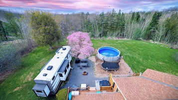 A recreational vehicle with a covered patio, a swimming pool, and a tree with pink blossoms.